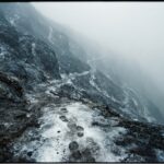 A steep, icy slope descending into fog with footprints vanishing below &mdash; representing a slippery slope argument's chain of assumed, unproven consequences