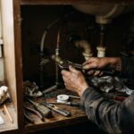 A pair of hands mid-repair under a sink — proof that trying it yourself, even messily, is never a waste of a weekend.